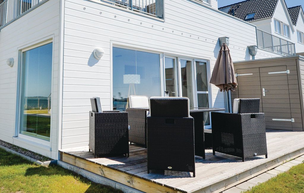 Holzterrasse mit schwarzen Stühlen und Tisch vor einem weißen Wohnhaus, Sonnenschirm an der Seite.