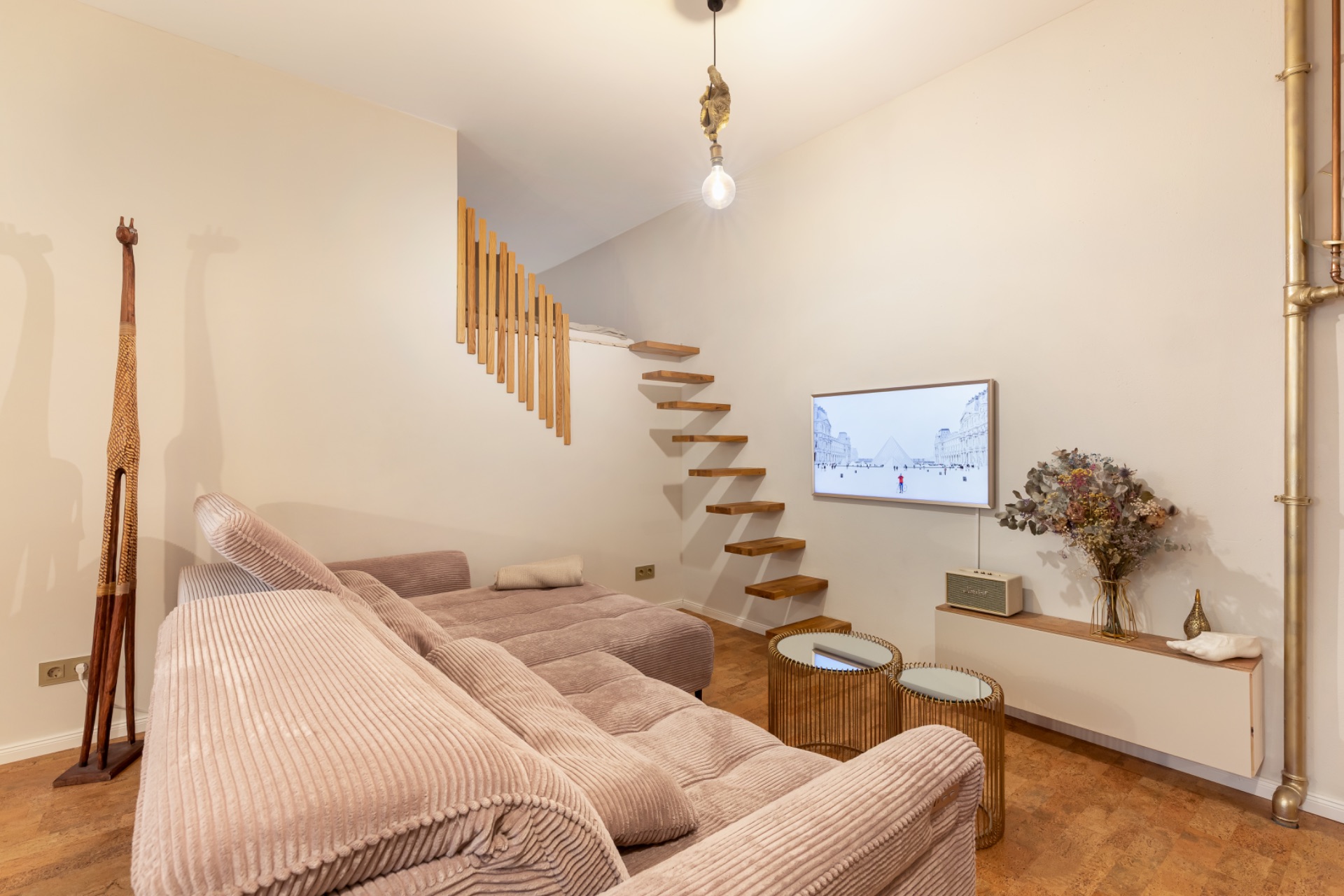 Wohnzimmer mit beigem Sofa, schwebender Holztreppe, Fernseher an der Wand und Dekoration.