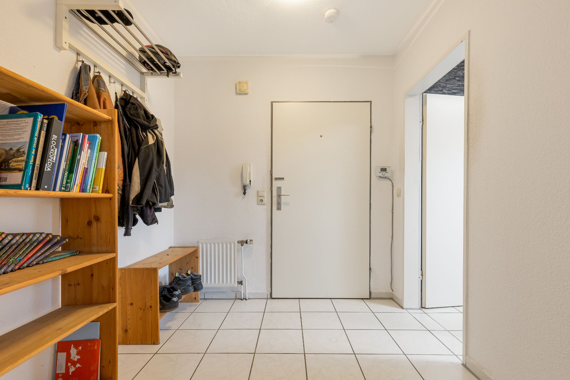 Heller Flur mit Bücherregal, Garderobe, Bank und weißer Eingangstür.