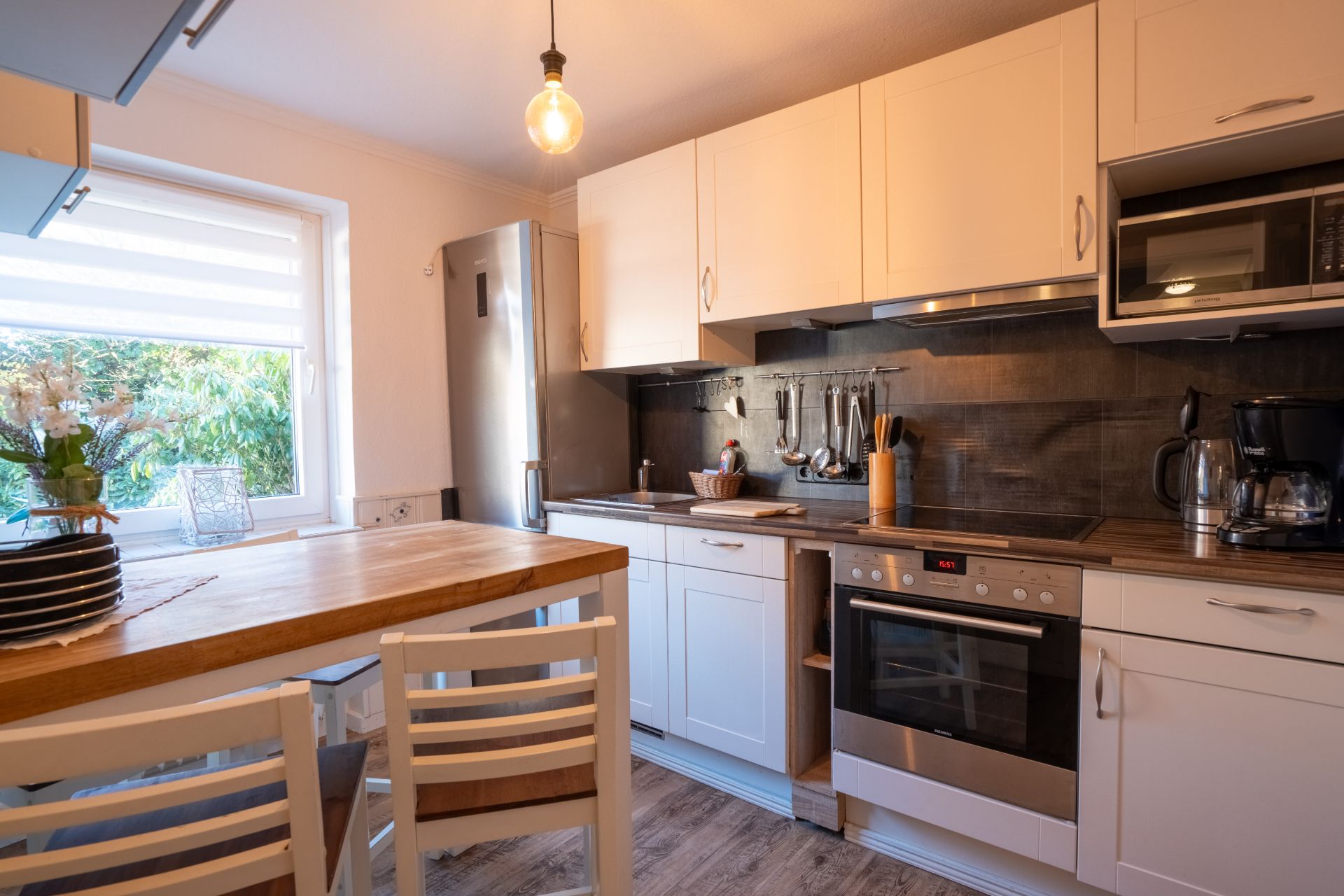 Moderne Küche mit Holztheke, weißen Schränken, Herd, Kühlschrank und großem Fenster.