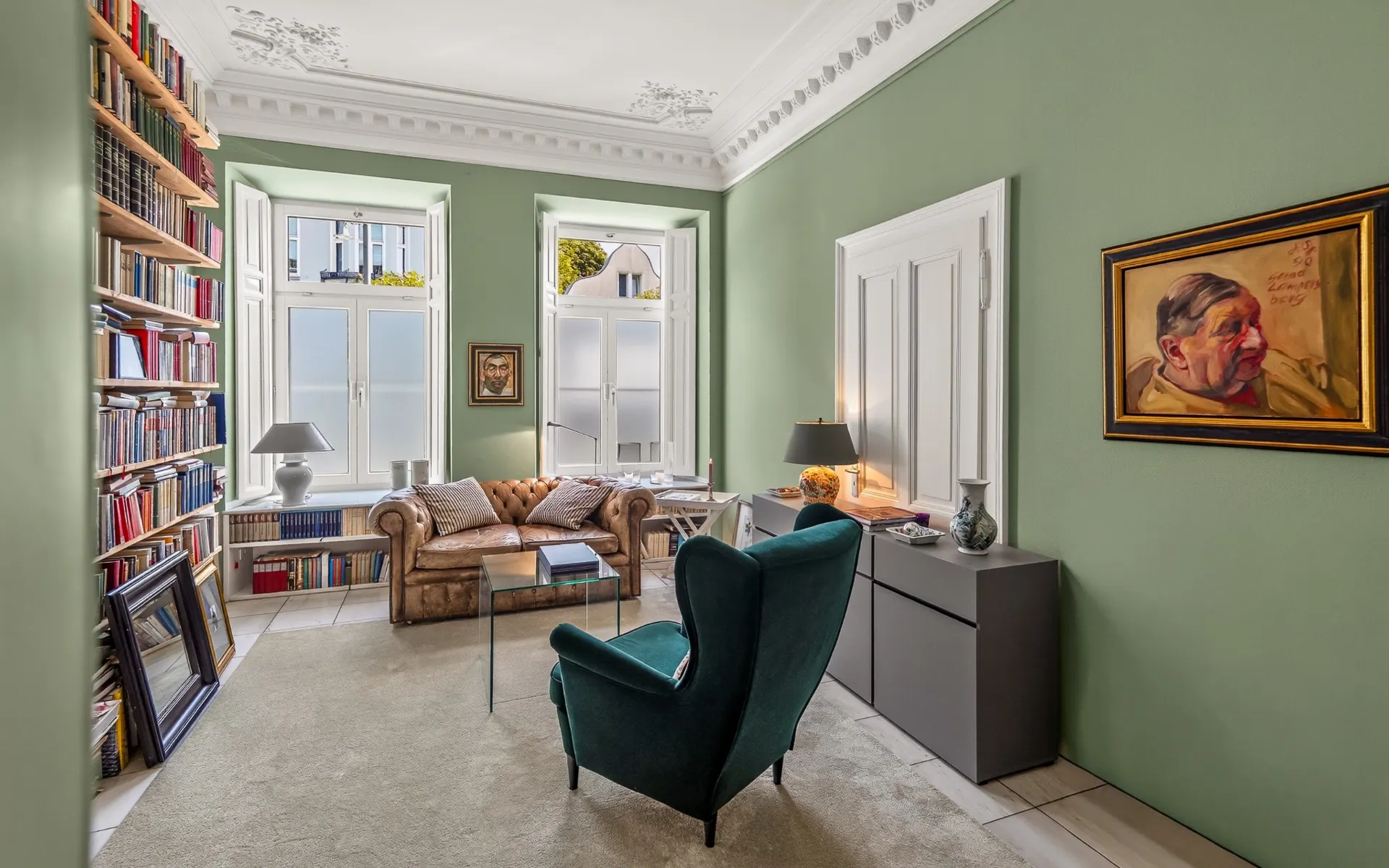 Helles Wohnzimmer mit Bücherregal, grünem Sessel, braunem Sofa und Gemälde an der Wand.