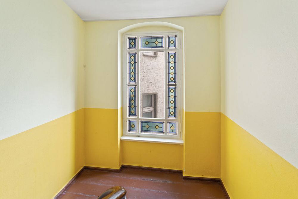 Kleiner Flur mit gelb-weißen Wänden und Fenster mit buntem Glasrand.