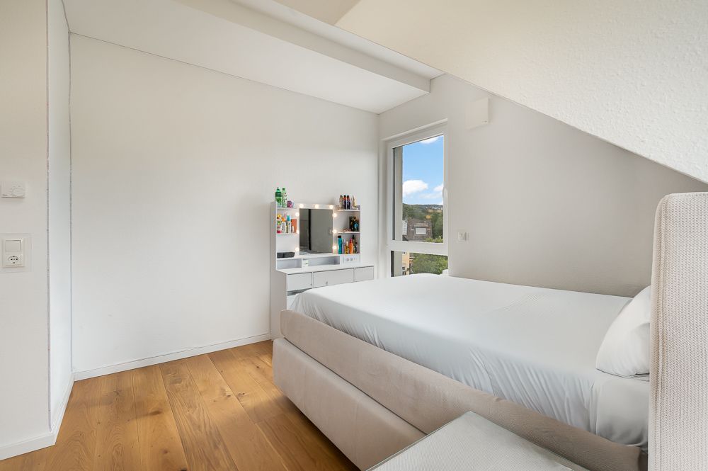 Helles Schlafzimmer mit Bett, Schminktisch und Fenster, Holzboden und weißen Wänden.