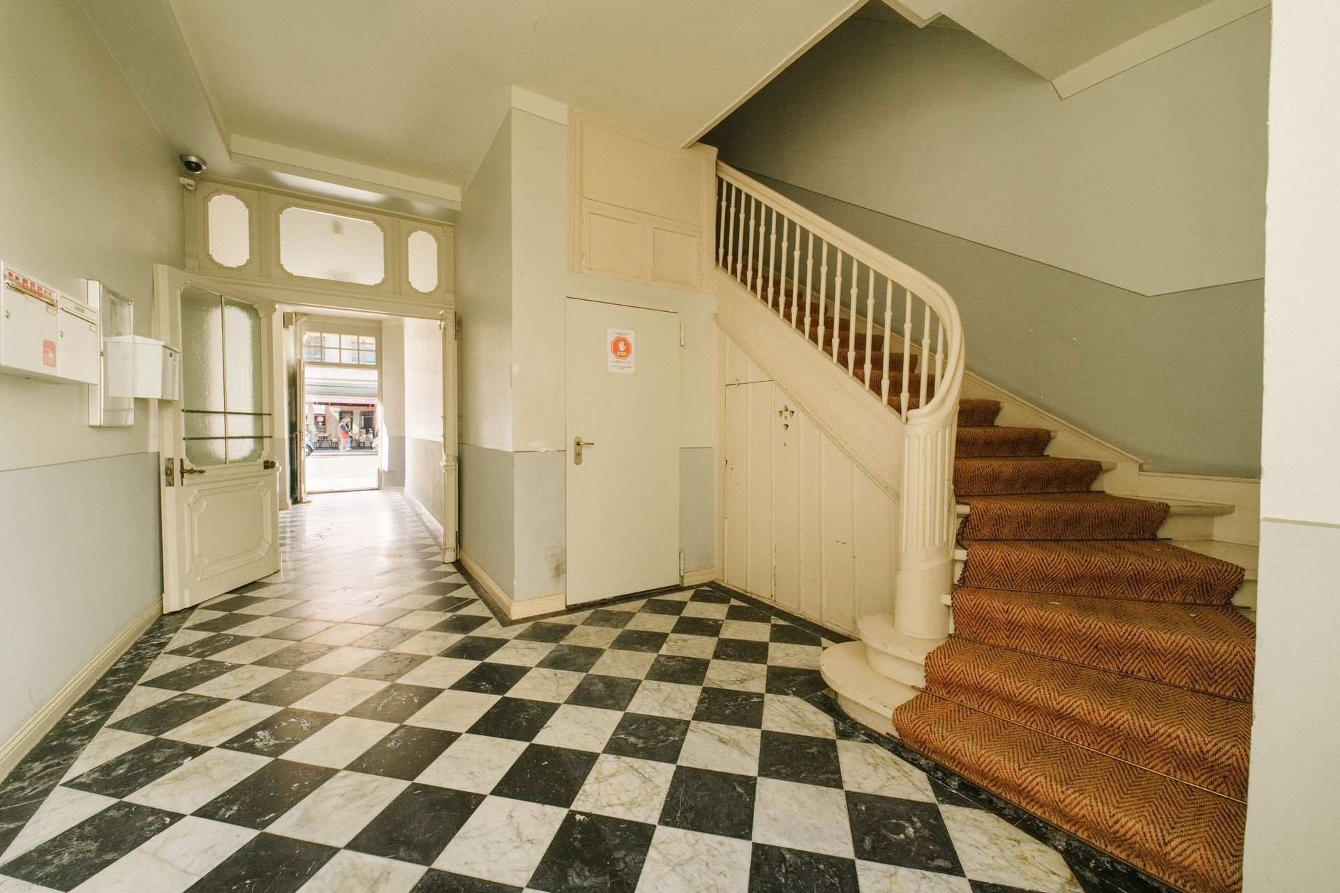 Eingangsbereich mit schwarz-weiß kariertem Boden und Treppe, offene Tür zum Außenbereich.