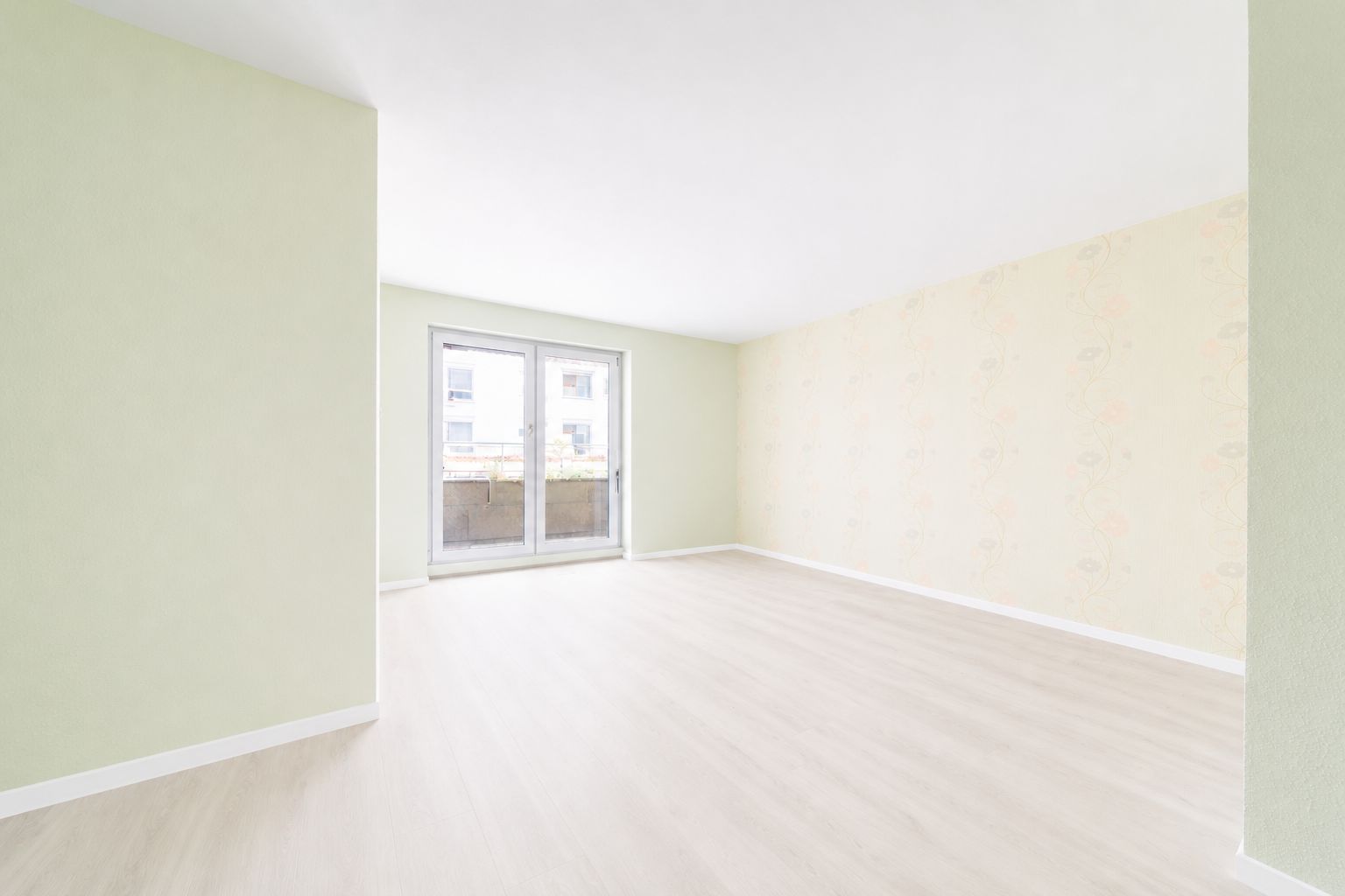 Heller leerer Raum mit großen Fenstern und hellem Holzboden.