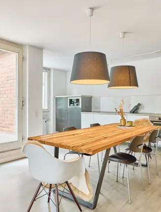 Heller Essbereich mit Holztisch, sechs Stühlen und offener weißer Küche im Hintergrund.