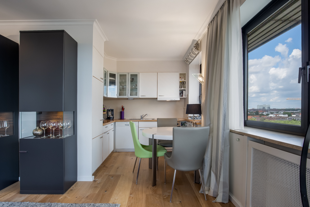 Moderne Küche mit weißem Schrank, Esstisch und großen Fenstern mit Blick nach draußen.