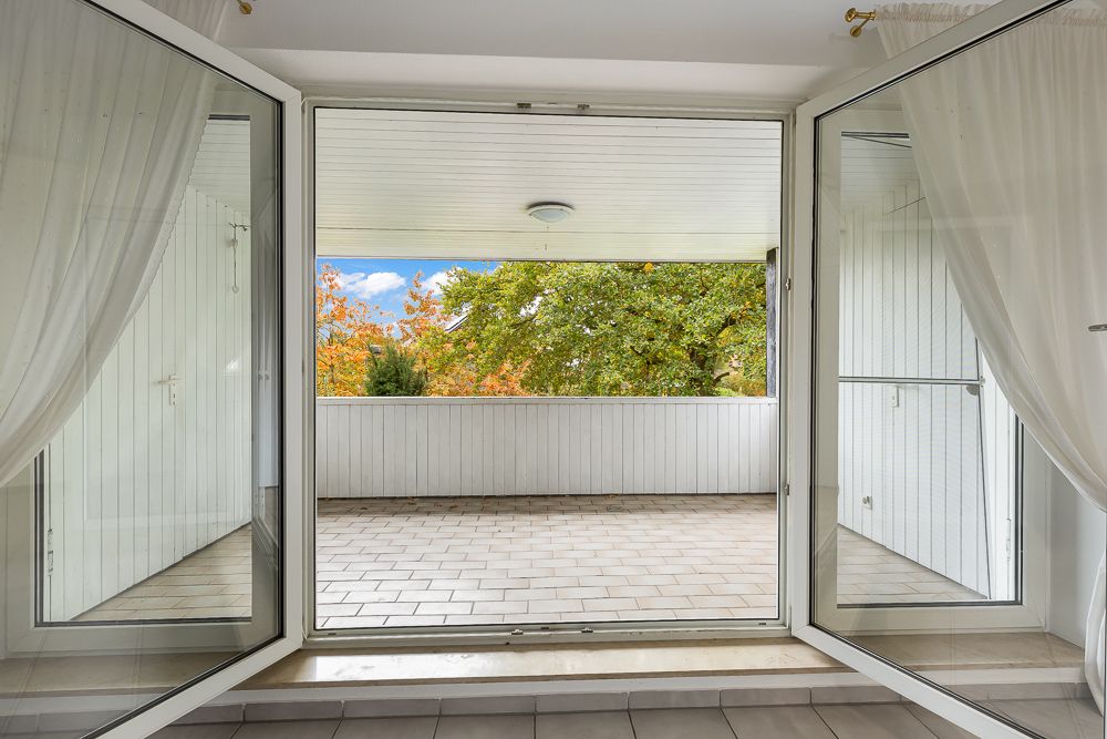 Offene Doppeltür führt auf einen überdachten Balkon mit Blick auf Bäume.