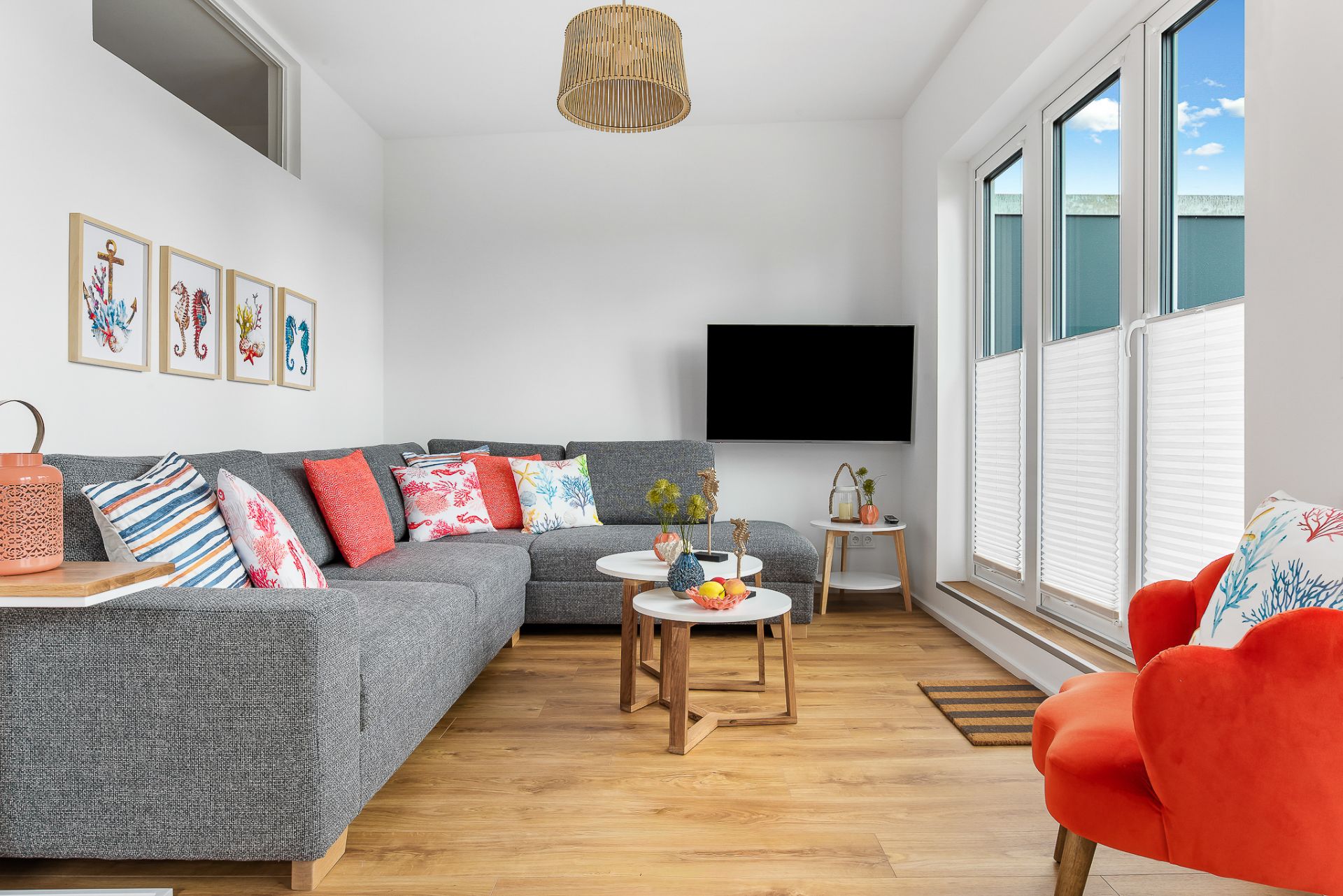 Modernes Wohnzimmer mit grauem Ecksofa, bunten Kissen, Flachbildfernseher und großen Fenstern.