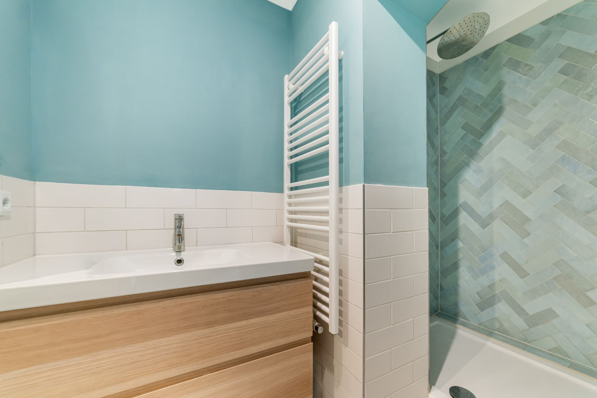 Modernes Badezimmer mit Waschbecken, Handtuchheizkörper und Dusche mit blauen Fliesen.