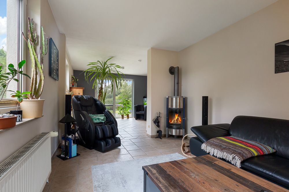 Wohnzimmer mit schwarzem Ledersofa, Holzofen, Massagesessel und vielen Pflanzen.