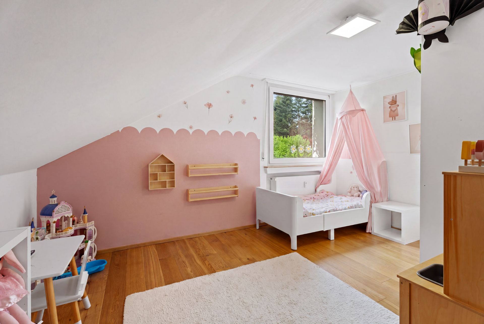 Helles Kinderzimmer mit Holzfußboden, Einzelbett mit Baldachin, Spielküche und Maltisch.