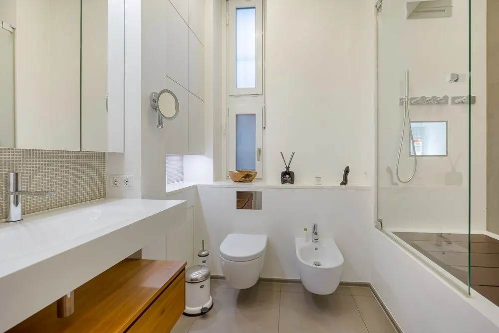 Modernes Badezimmer mit Waschbecken, Toilette, Bidet, Dusche und Fenster.