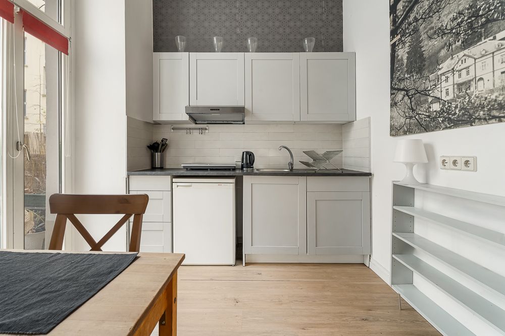 Helle Küche mit weißen Schränken, kleinem Kühlschrank und Esstisch mit Stuhl.