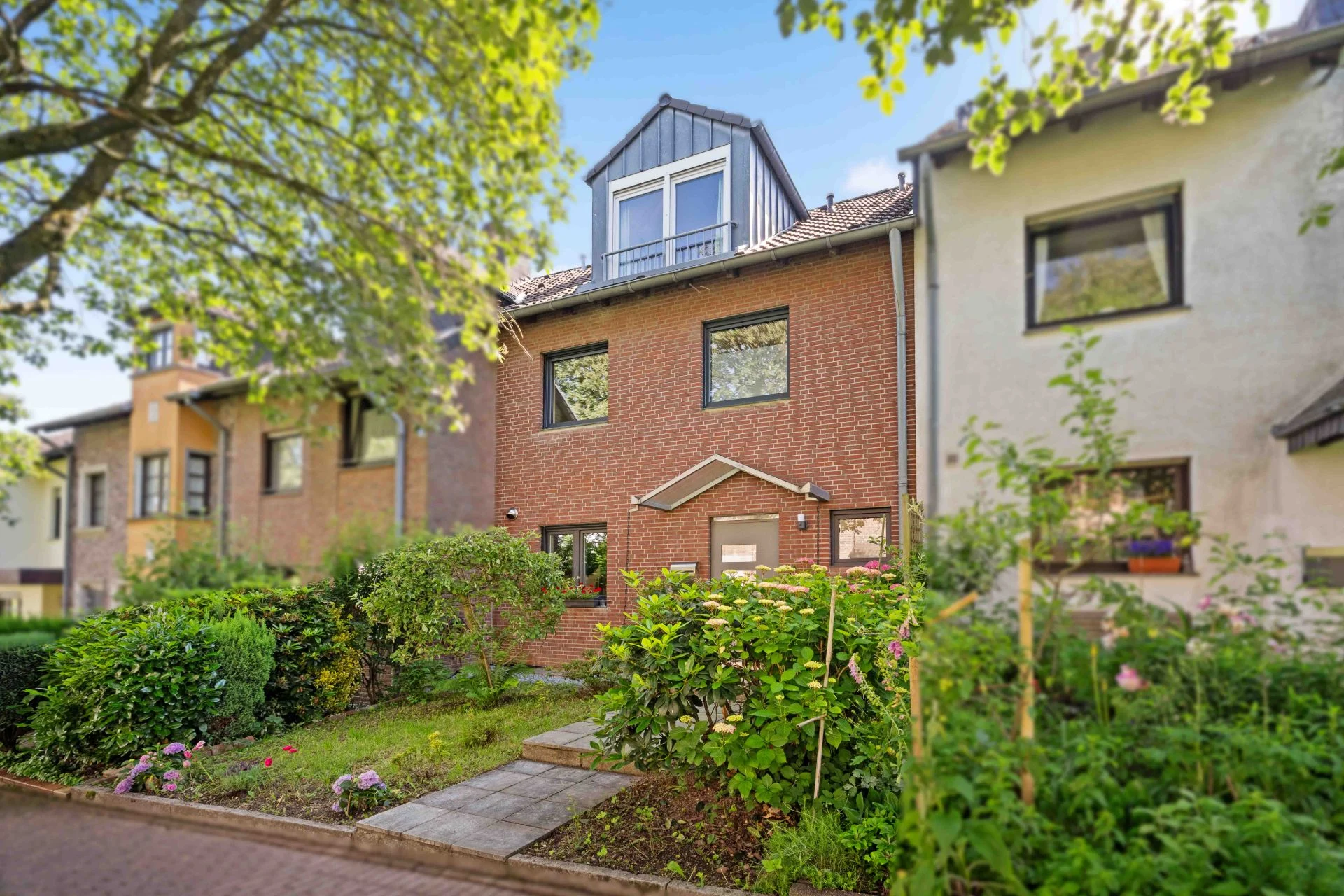Vorderansicht eines roten Reihenhauses mit Vorgarten und Bäumen.