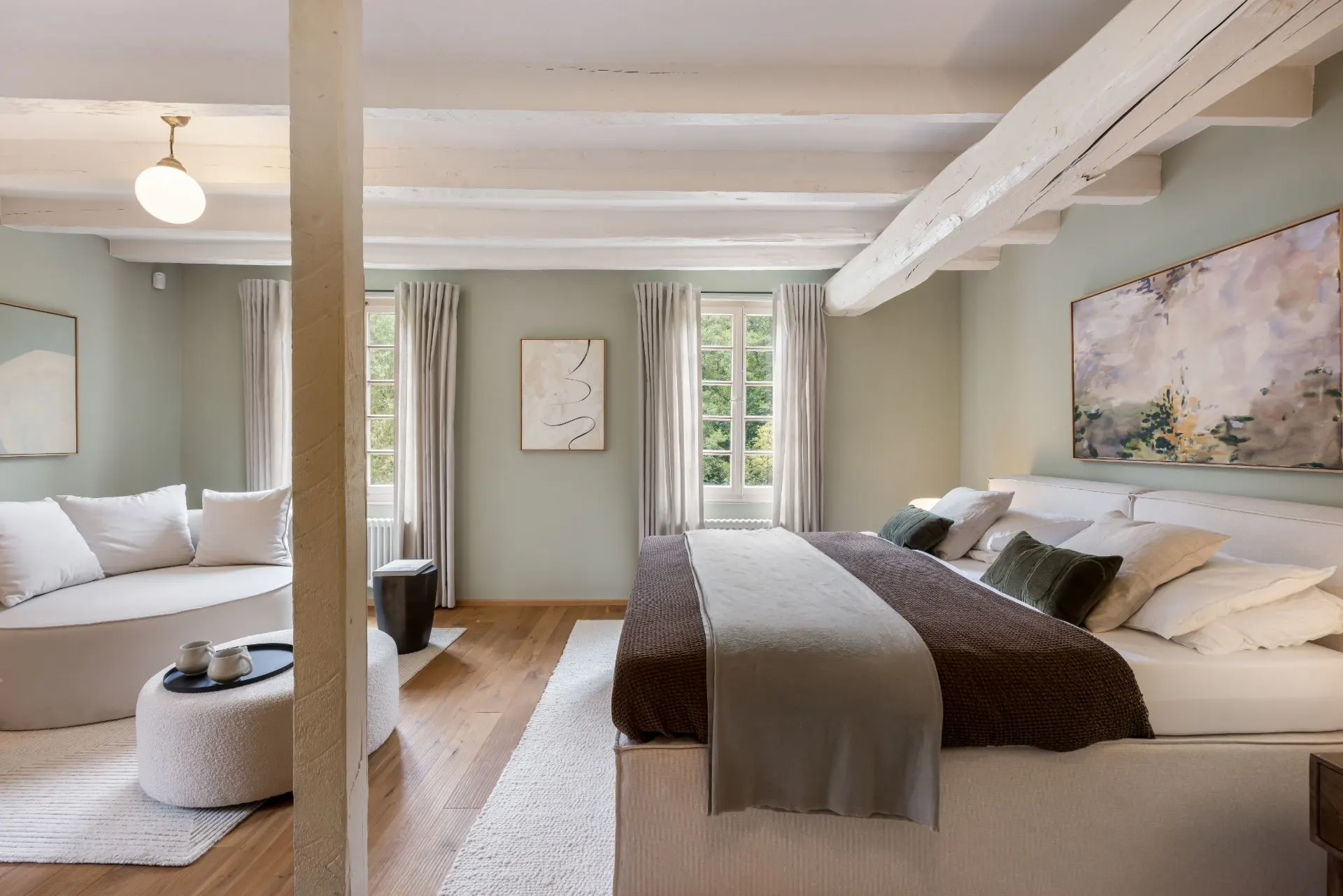 Helles Schlafzimmer mit Doppelbett, Sofa, zwei Fenstern, Holzdecke und moderner Dekoration.