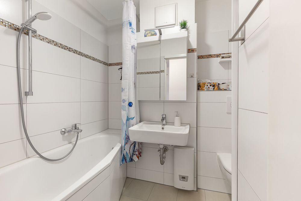 Modernes Bad mit Badewanne, Duschvorhang, Waschbecken, Spiegel und WC.