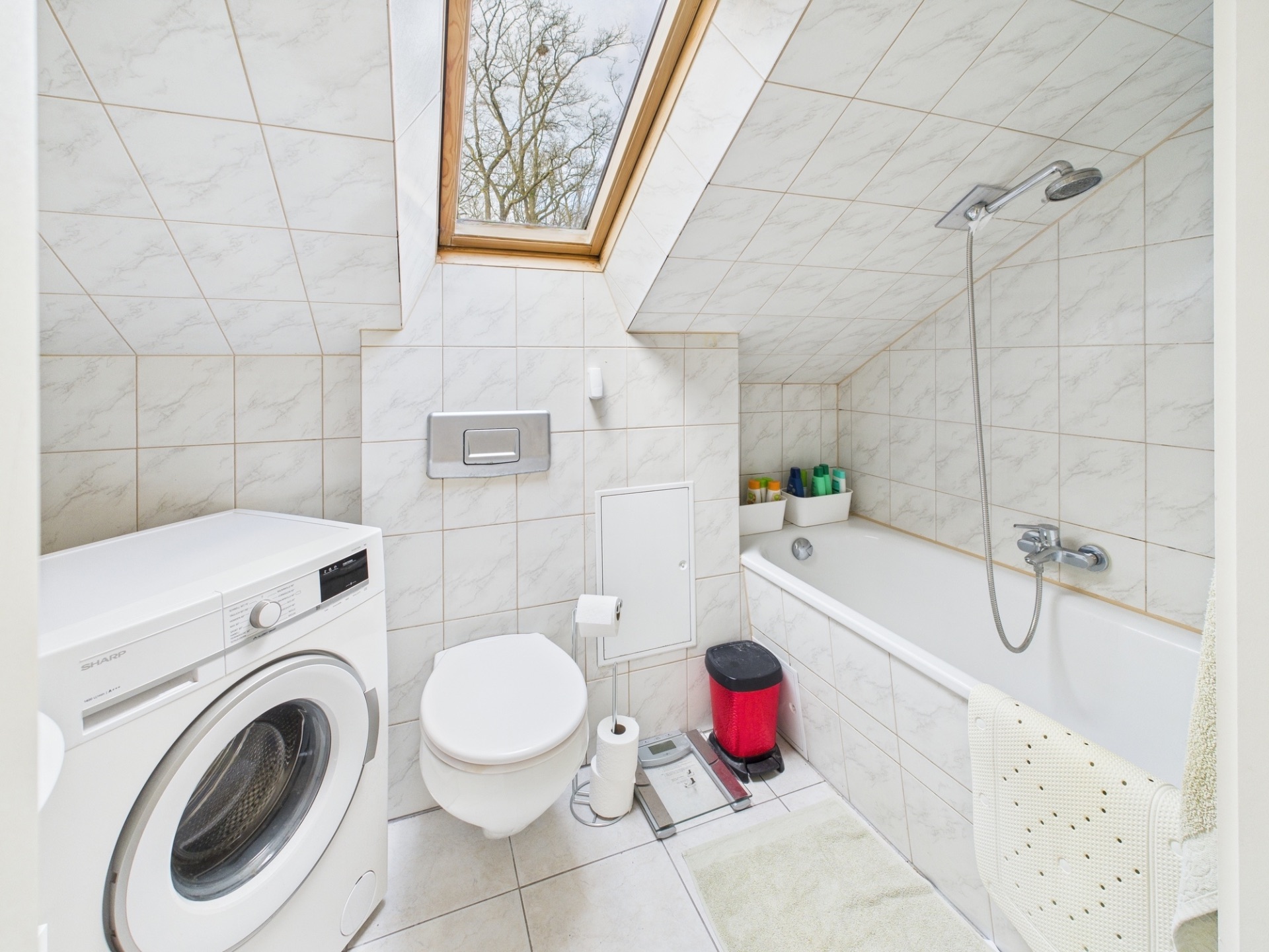 Helles Badezimmer mit Waschmaschine, Toilette, Badewanne und Dachfenster.