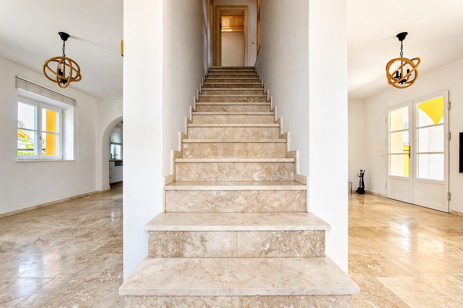 Helle Eingangshalle mit Marmortreppe, Fliesenboden und zwei modernen Hängelampen.