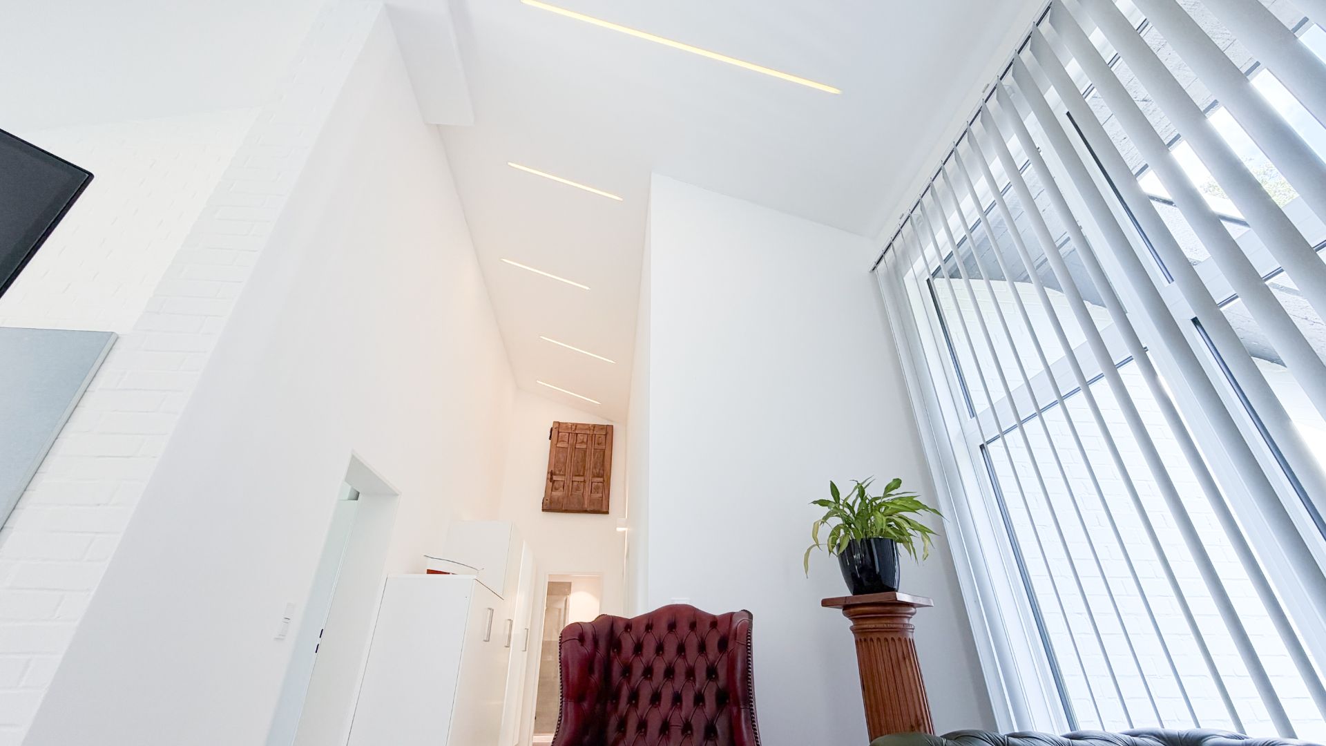 Helles Wohnzimmer mit hohen Decken, Fensterjalousien und rotem Sessel.