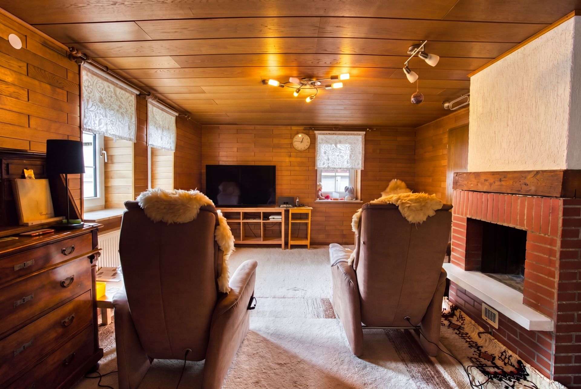 Wohnzimmer mit zwei Sesseln, Kamin, Fernseher und Holzvertäfelung.