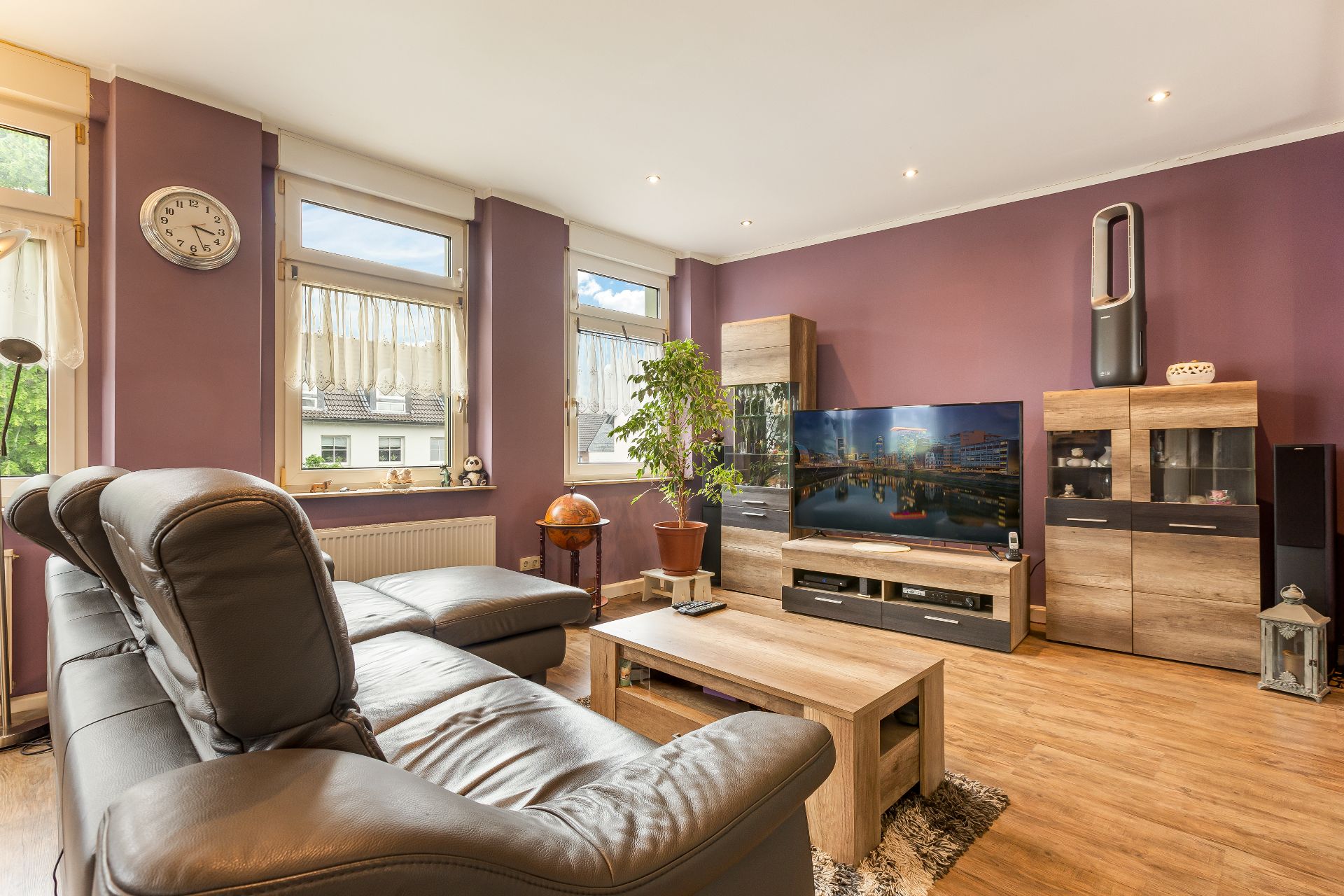 Modernes Wohnzimmer mit Leder-Sofa, Couchtisch, Fernseher und lila Wand.