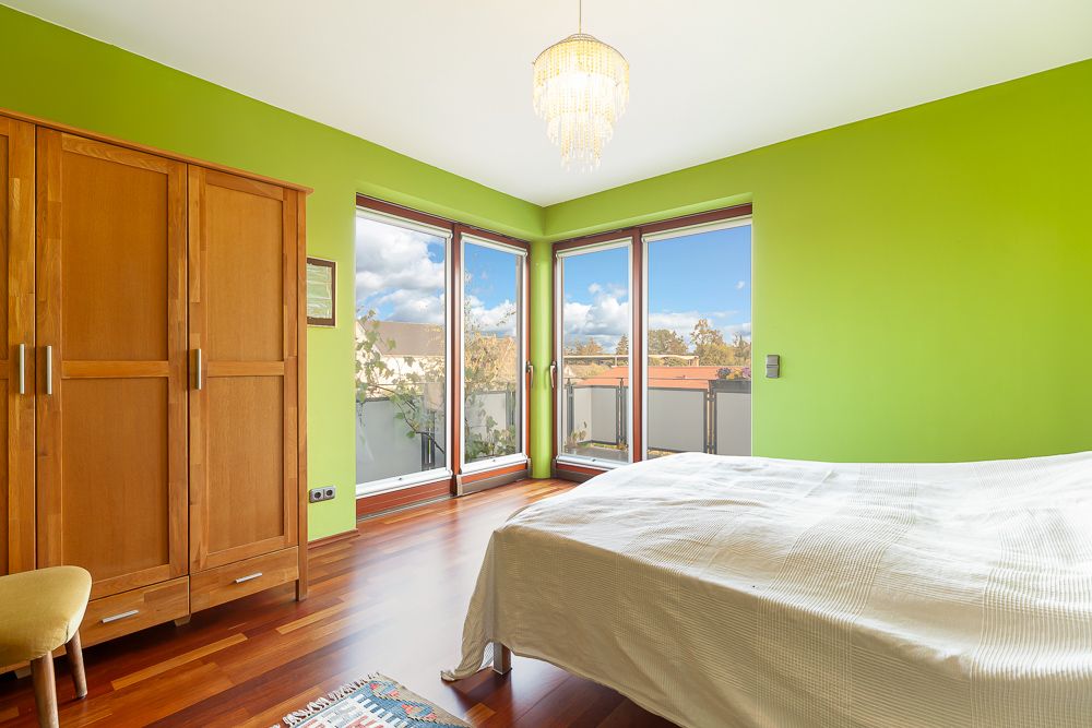 Helles Schlafzimmer mit grüner Wand, Holzschrank, Bett und großen Fenstern mit Balkonzugang.