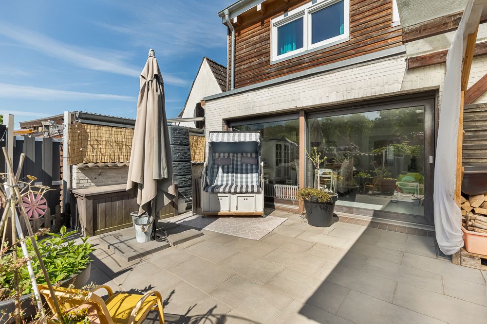Sonnige Terrasse mit Strandkorb, Sonnenschirm und Pflanzen vor einem Wohnhaus.