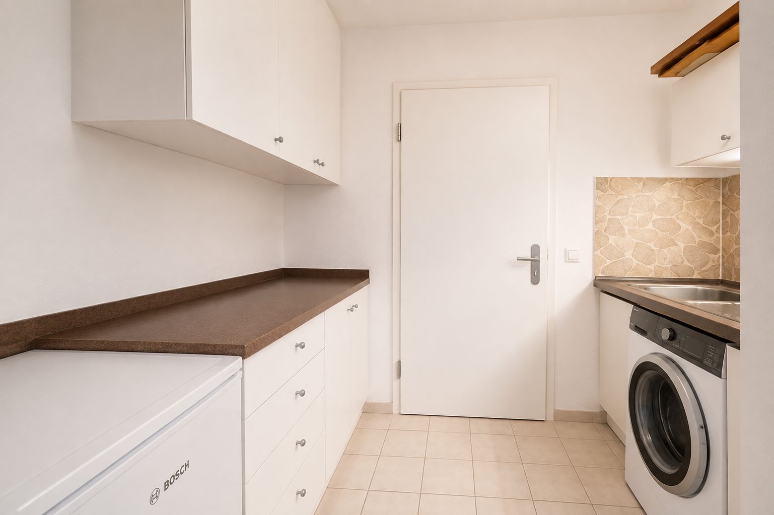 Heller Hauswirtschaftsraum mit Waschmaschine, Arbeitsplatten und weißen Schränken.