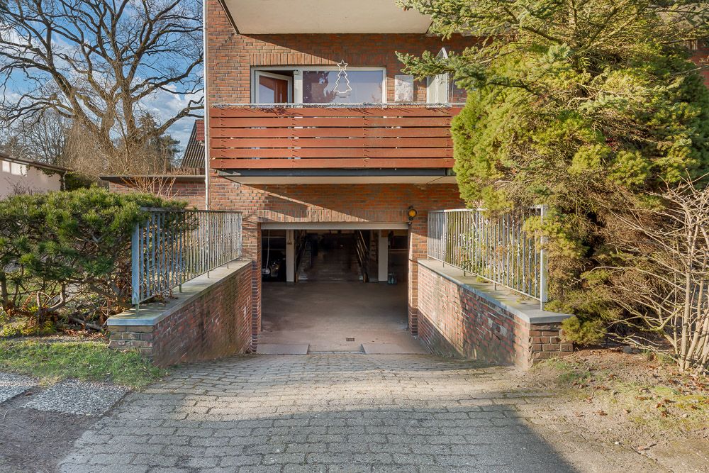 Zufahrt zu einer Tiefgarage unter einem Wohnhaus mit roten Backsteinwänden und umliegenden Büschen.