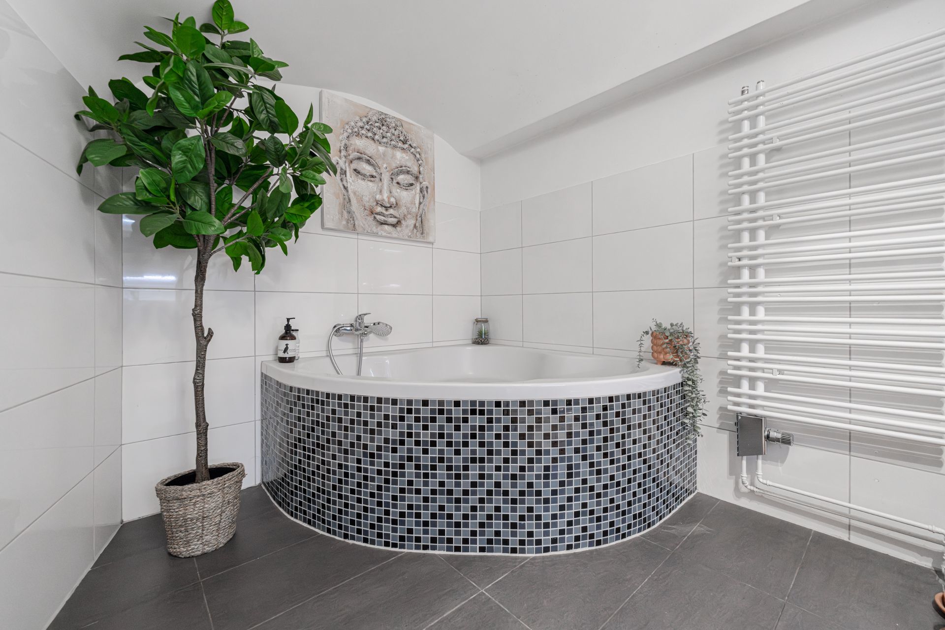 Ecke mit Badewanne, Mosaikfliesen, Topfpflanze und Wandbild in modernem Badezimmer.