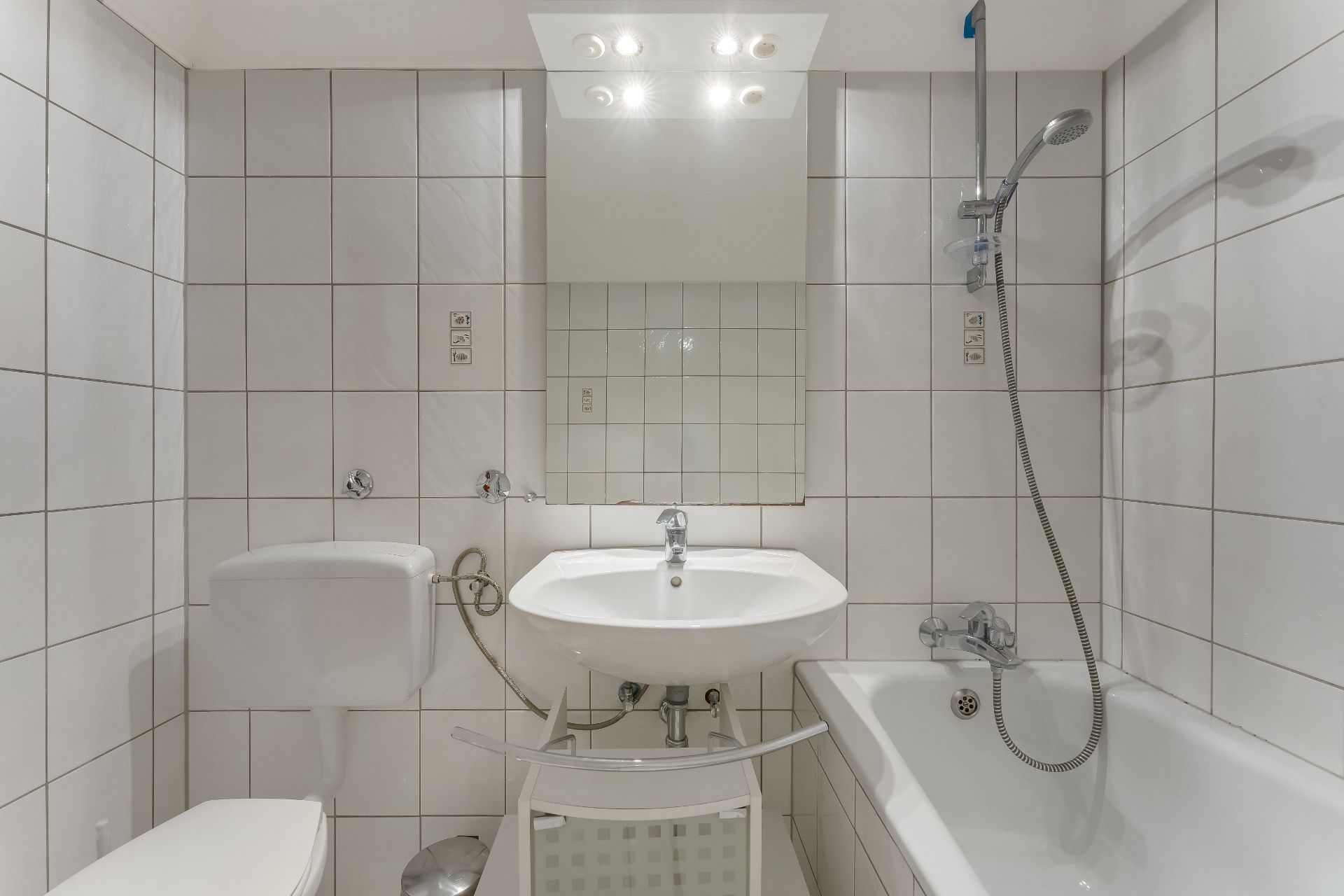 Modernes Badezimmer mit weiß gefliesten Wänden, Waschbecken, Spiegel, Toilette und Badewanne mit Dusche.