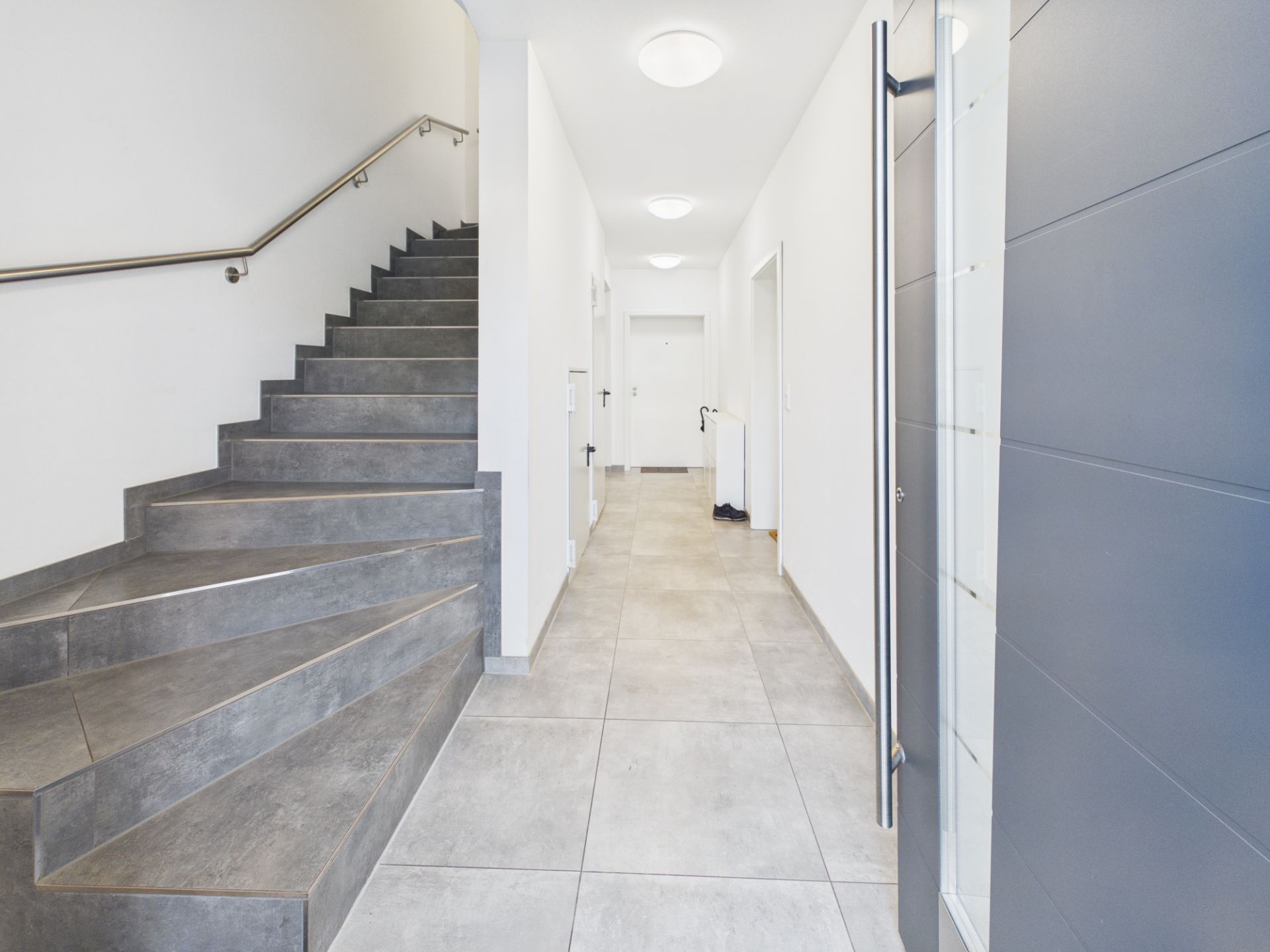 Heller Flur mit grauer Treppe und Fliesenboden in einem Wohnhaus.