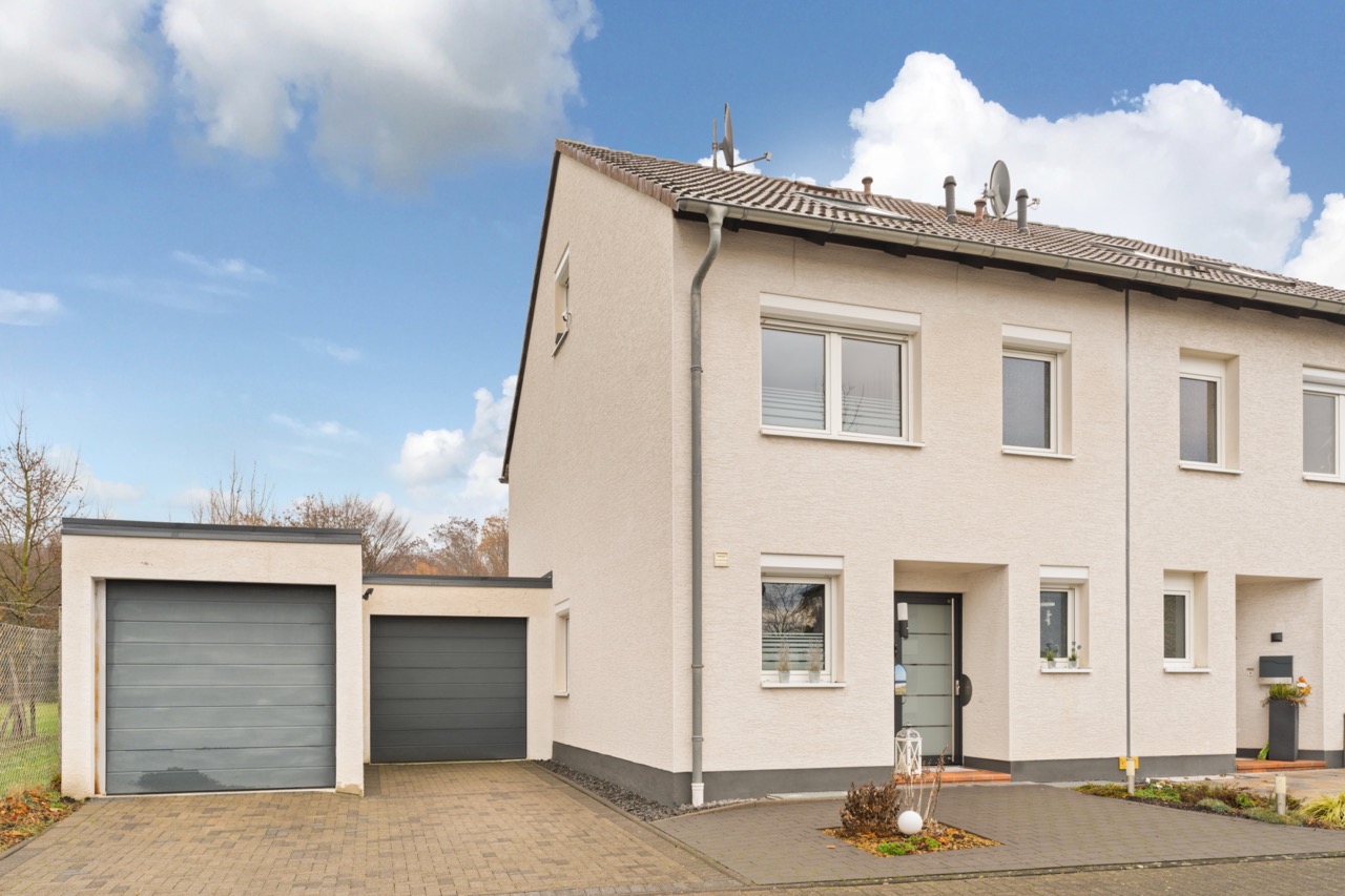 Helles Reihenhaus mit Garage, gepflasterter Einfahrt und kleinem Vorgarten.