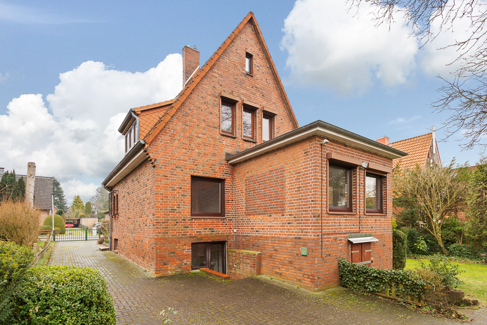 Backsteinwohnhaus mit Satteldach und Anbau, umgeben von Garten und gepflastertem Weg.