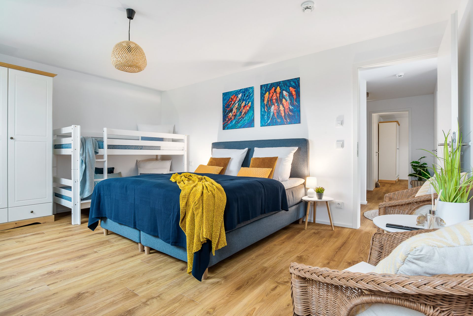 Helles Schlafzimmer mit Doppelbett, Etagenbett, Kleiderschrank und Sitzbereich auf Holzfußboden.
