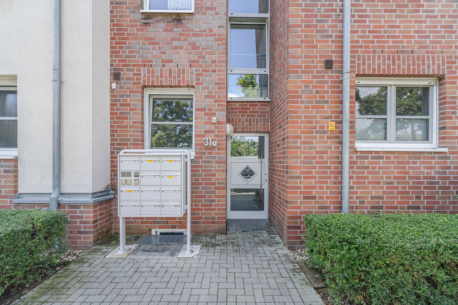 Eingang eines Wohnhauses aus rotem Backstein mit Briefkästen und Hecke davor.