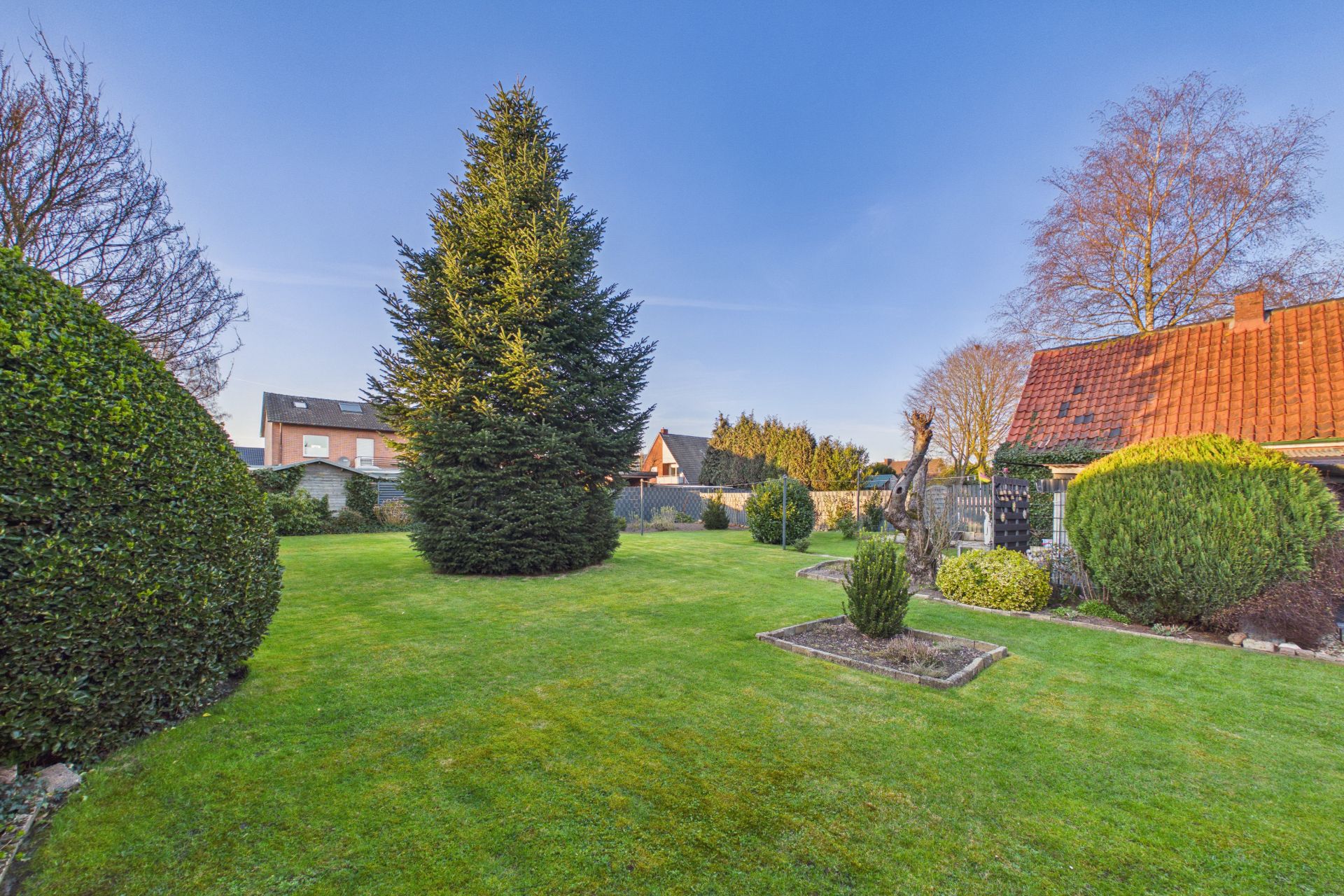 Großer Garten mit Rasen, Büschen, Bäumen und einem Haus mit rotem Dach rechts.