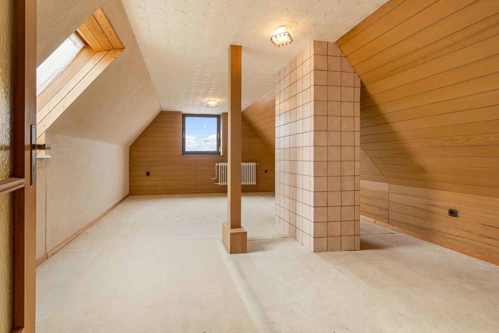 Dachgeschossraum mit Holzverkleidung, Fenster, Heizkörper und Fliesenpfeiler.