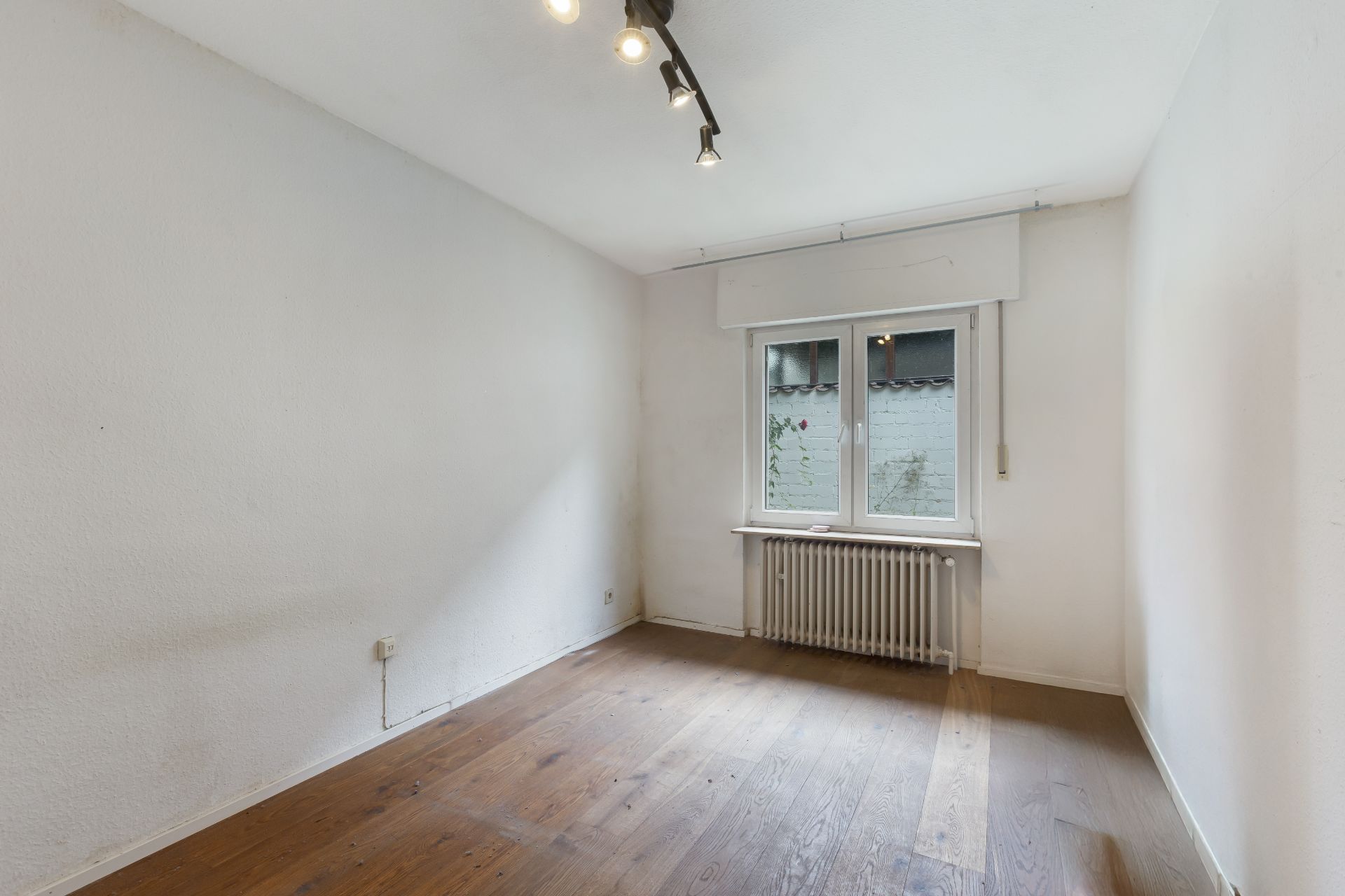 Leerer Raum mit Holzfußboden, weißer Wand, Fenster und Heizkörper unter dem Fenster.