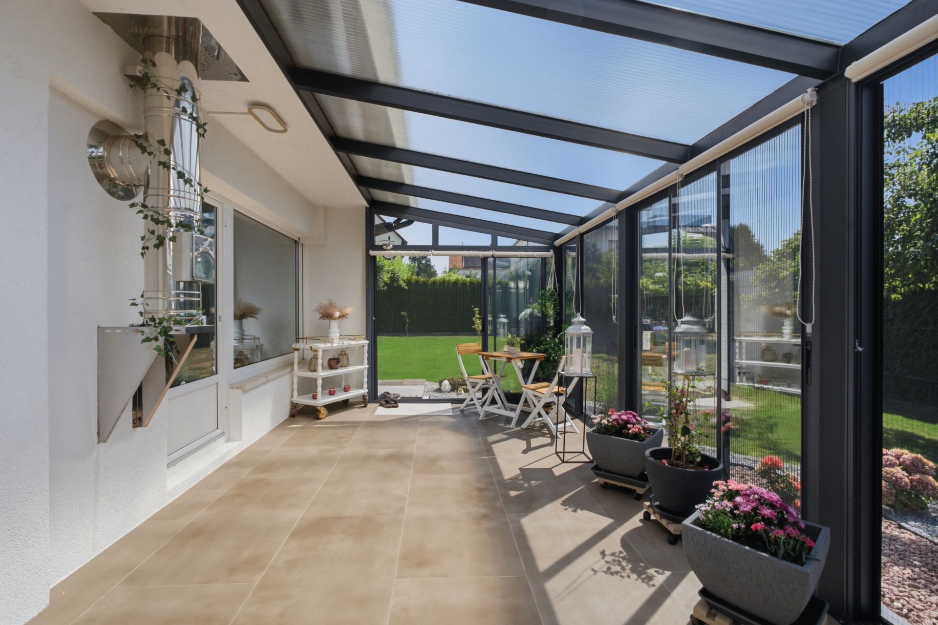 Wintergarten mit Glasdach, Sitzgruppe, Pflanzen und Blick auf den Garten.