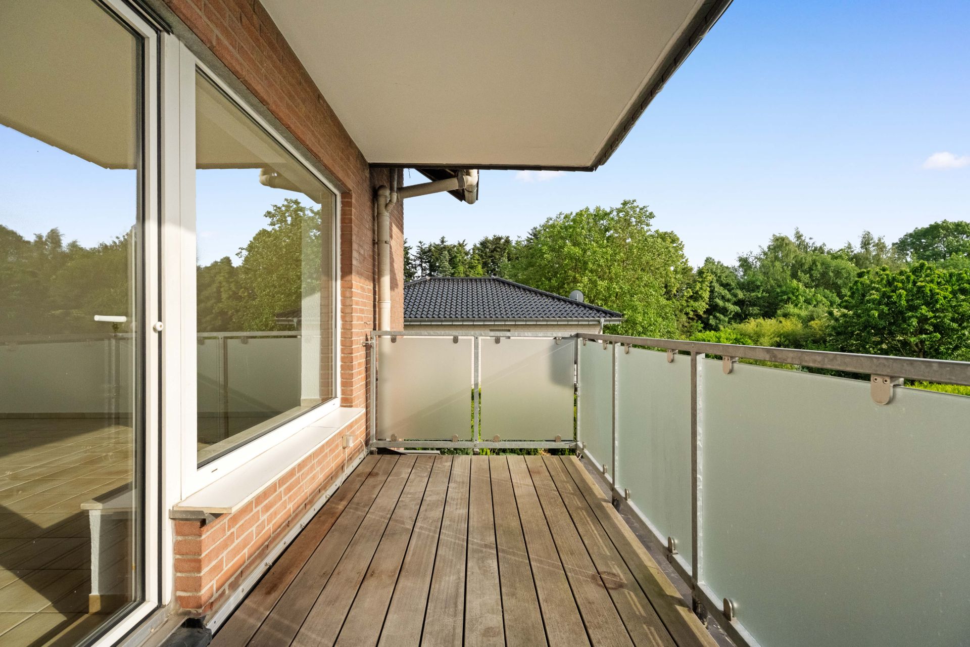 Moderner Balkon mit Holzfußboden, Glasgeländer und Blick ins Grüne.