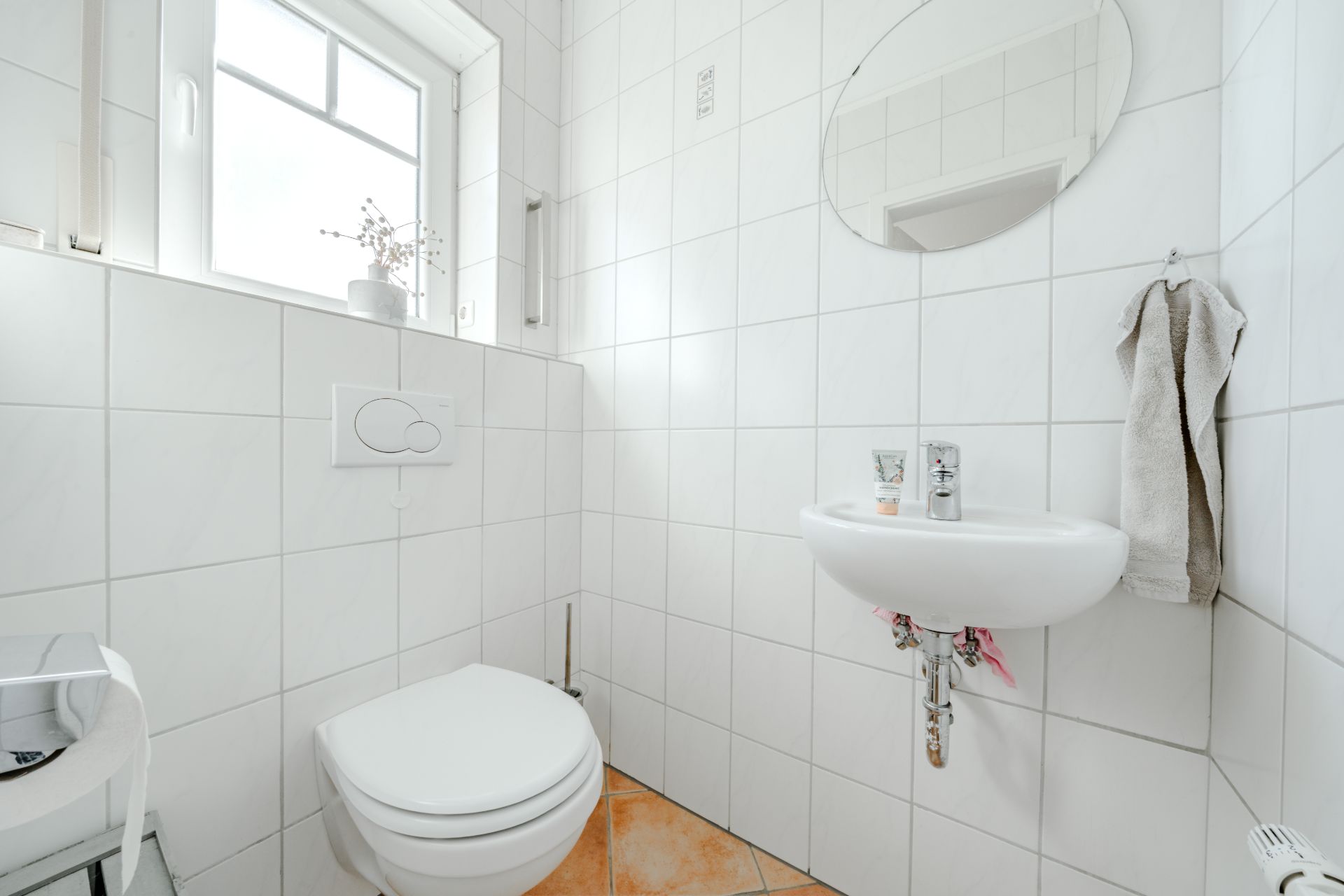 Helles Badezimmer mit WC, kleinem Waschbecken, Spiegel und Fenster.