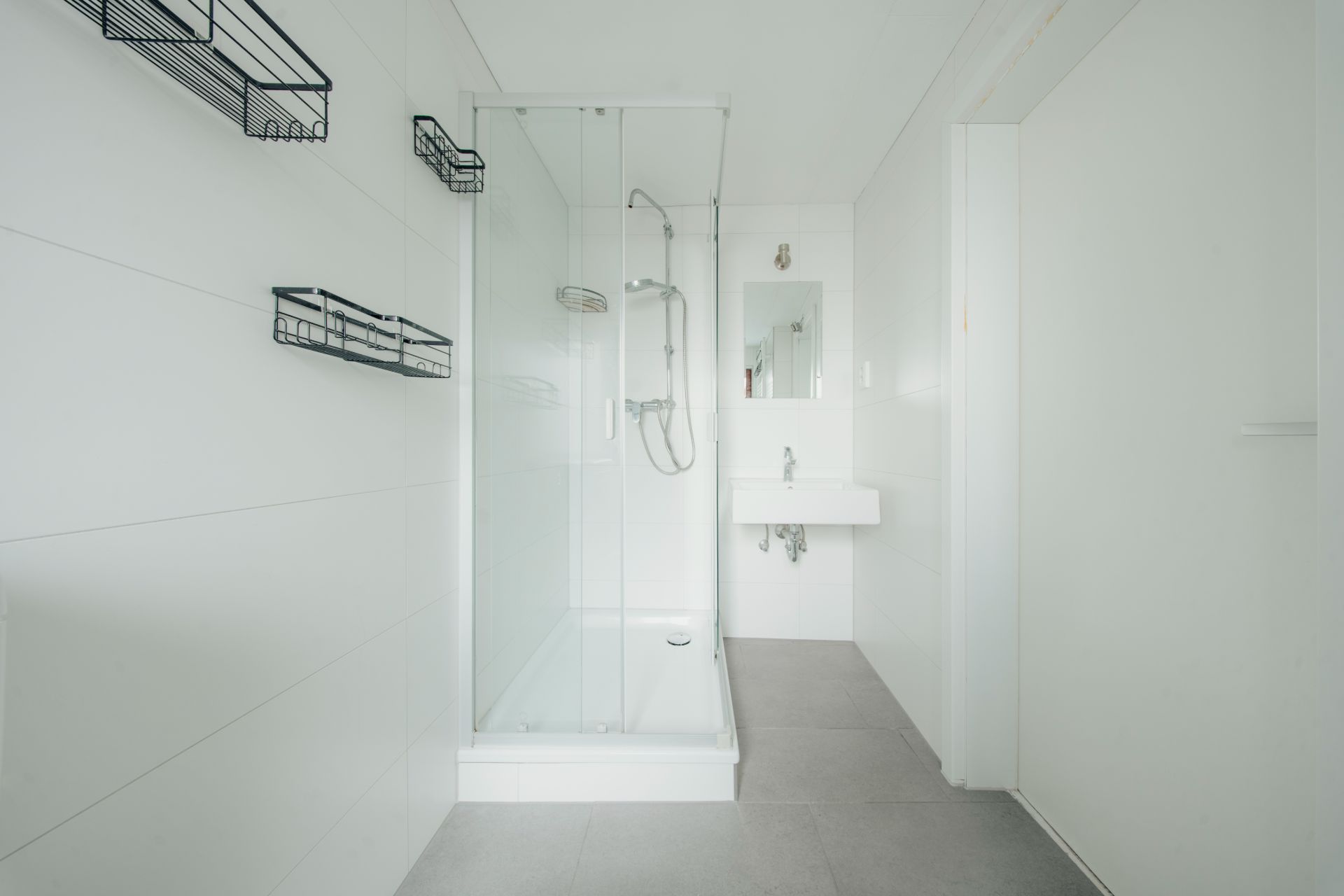 Helles Badezimmer mit Glasdusche, Waschbecken, Spiegel und Wandregalen.