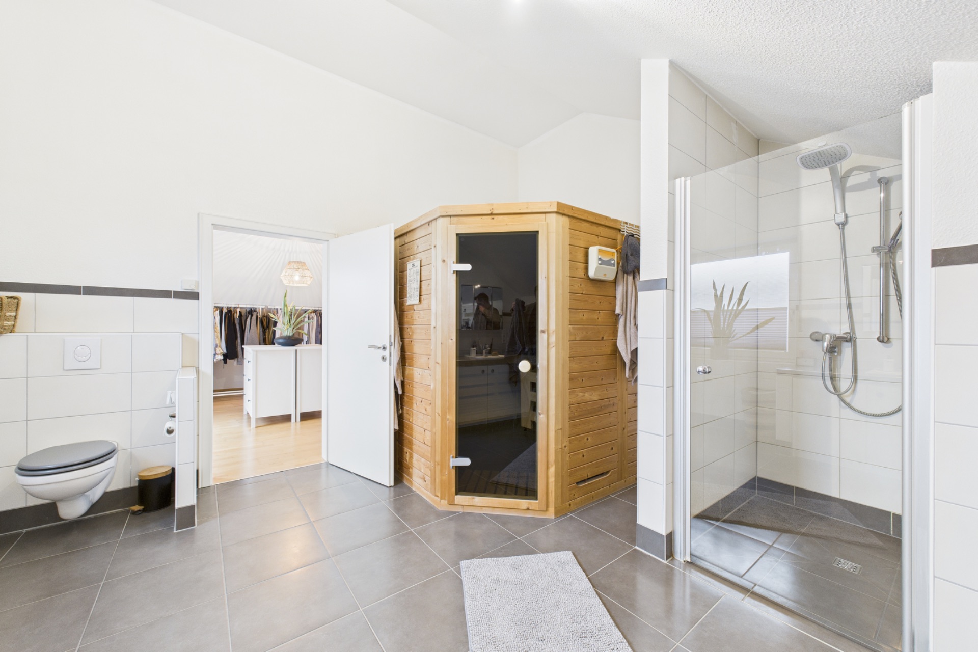 Modernes Badezimmer mit Sauna, Dusche, WC und Zugang zu einem Ankleidezimmer.