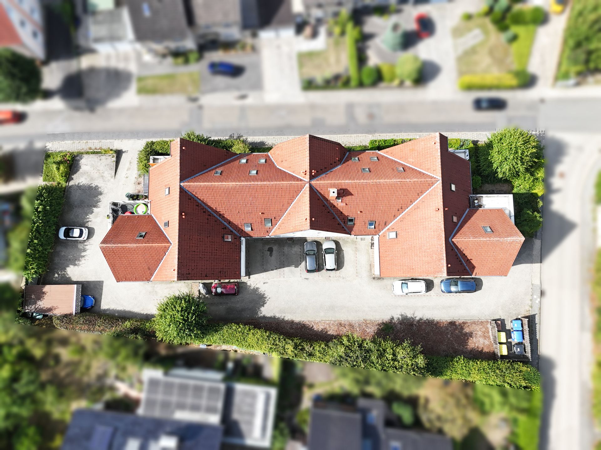 Luftaufnahme eines Wohngebäudes mit rotem Dach, Zufahrt und mehreren geparkten Autos.