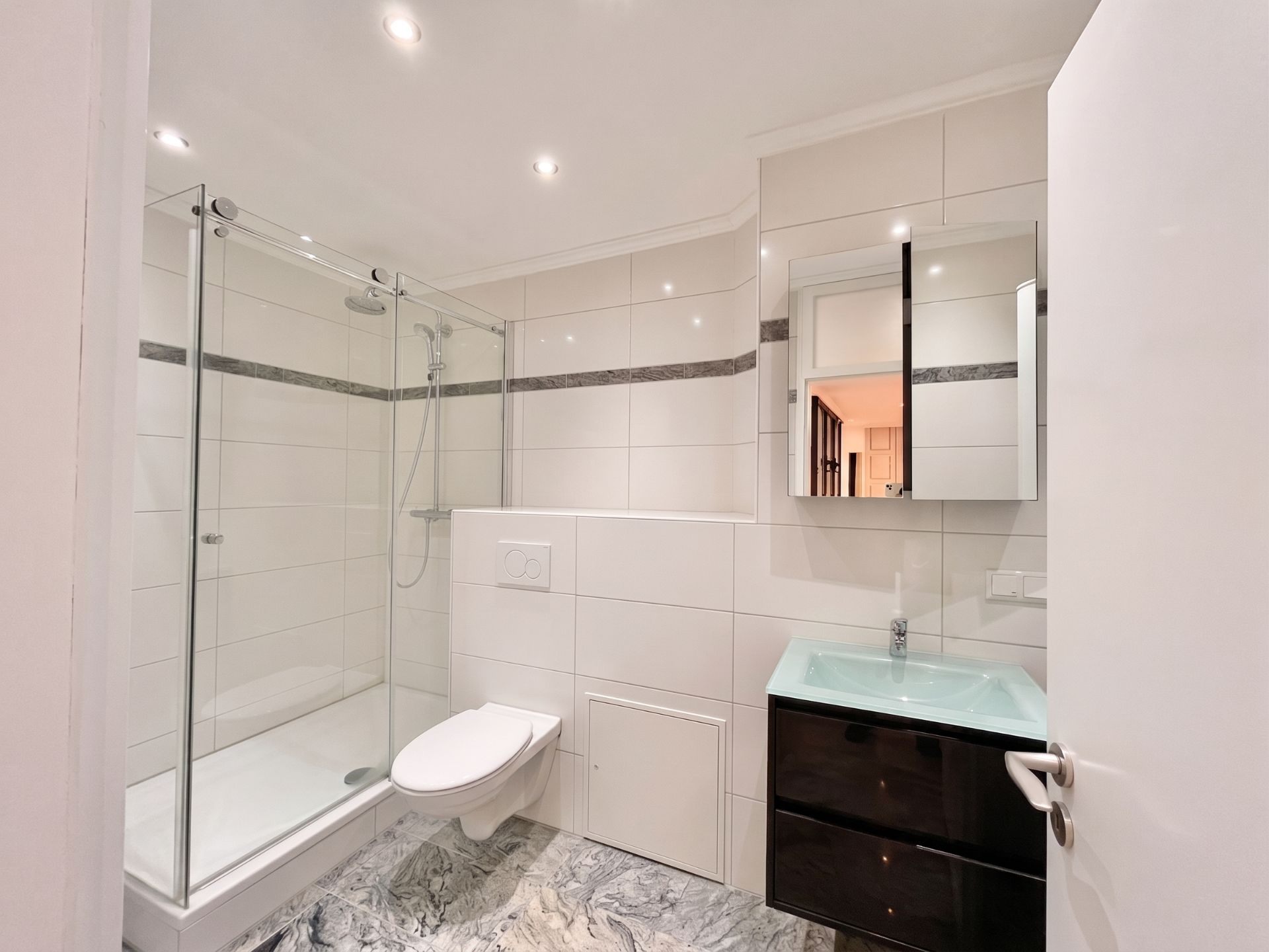 Modernes Badezimmer mit großer Dusche, Wandtoilette und Waschbecken mit Spiegel.