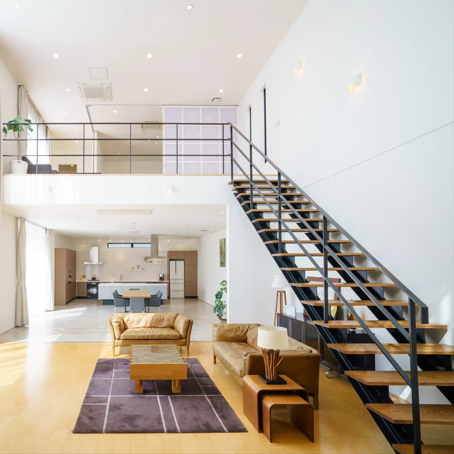 Modernes Wohnzimmer mit offener Küche, braunen Sofas und einer Treppe zur oberen Etage.