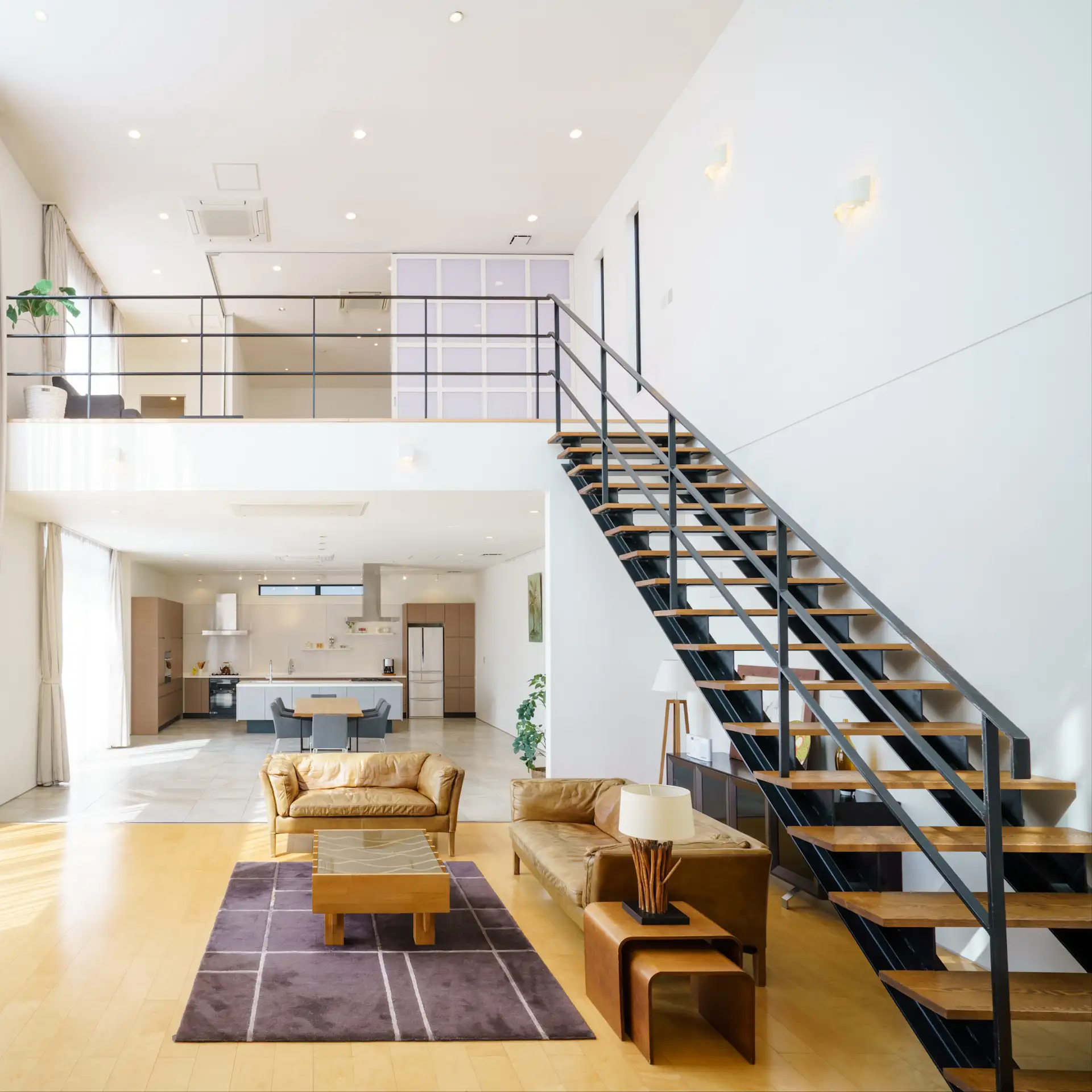Modernes Wohnzimmer mit offener Küche, braunen Sofas und einer Treppe zur oberen Etage.