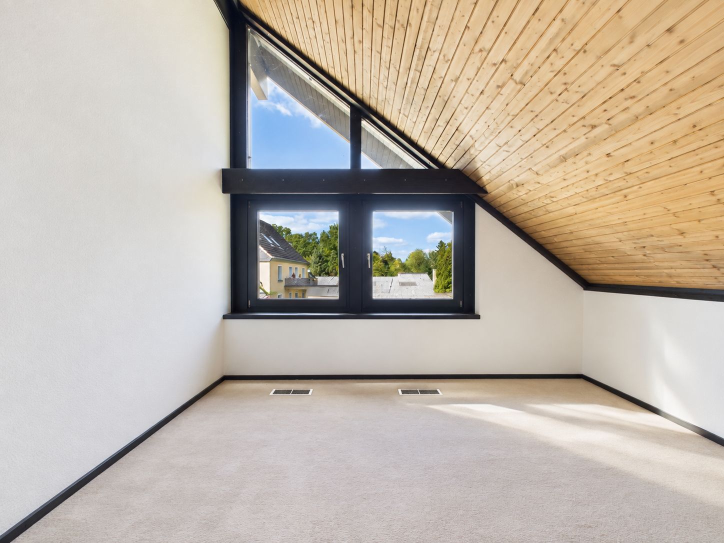 Leerer Dachraum mit schräger Holzdecke und großem Fenster.